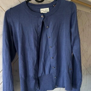 Blå kofta från Holly & White - Säljer en stilren blå kofta från Holly & White. Den har långa ärmar och knappar framtill. Perfekt för lager-på-lager och passar till många olika outfits. Mjukt material som känns skönt mot huden.