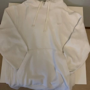 Vit Nike hoodie  - Säljer en stilren vit hoodie från Nike. Den har en klassisk design med en stor ficka framtill och justerbar huva. Perfekt för en avslappnad look. 🏷️