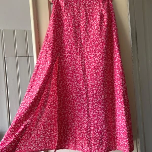 Rosa blommig långkjol från SHEIN - Superfin långkjol från SHEIN i starkt rosa med vitt blommönster. Kjolen har en flowy passform och dragkedja bak. Perfekt för dig som vill sticka ut med färg och mönster. Materialet känns lätt och luftigt, perfekt för varmare dagar.