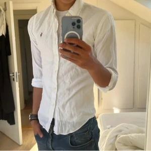 Ralph Lauren skjorta - Klassisk vit skjorta från Ralph Lauren med lång ärm och knappar framtill. Skjortan har den ikoniska broderade loggan på bröstet och är tillverkad i bomull. Perfekt för en clean och stilren look.