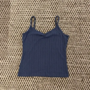 Kappahl mörkblå ribbad linnetopp - Säljer en mörkblå ribbad linnetopp med smala axelband och lätt rynk vid bysten. Toppen har en slim passform och är tillverkad i mjuk bomull. Använd bara en enstaka gång och köptes för 199kr. Skicket är 10/10. Skriv gärna om ni har några frågor!!
