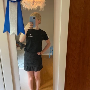 Glittrig svart kjol från Kappahl - Supersnygg svart kortkjol från Kappahl med glittriga detaljer och volang nertill. Kjolen har en tight passform och är perfekt för dig som gillar att sticka ut lite extra. Stretchigt material som sitter skönt på kroppen.