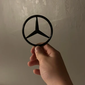 Mercedes-Benz emblem svart - Säljer en svart Mercedes-Benz emblem i metall med den klassiska treuddiga stjärnan. Perfekt som accessoar eller dekoration för dig som gillar bilar och vill ha något unikt.