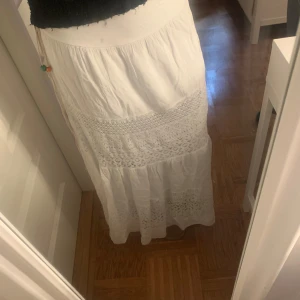 Vit långkjol med spets från Italy Moda - Superfin vit långkjol från Italy Moda med broderade spetsdetaljer och volanger. Kjolen har en bohemisk känsla och ett knytband med färgglada pärlor. Nyskick❣️