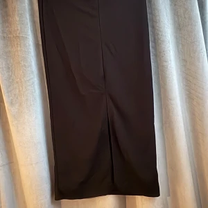 Svart långkjol med slits - En stilren svart långkjol med rak passform och diskret slits baktill. Perfekt för dig som gillar minimalistisk och clean stil. Kjolen är enkel att matcha och funkar till många olika looks.