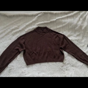 Brun croppad polotröja - Mysig brun polotröja med croppad passform och ribbad hals. Perfekt för lager-på-lager och passar till både jeans och kjol. Långärmad och stickad i mjukt material som håller dig varm under kyliga dagar.