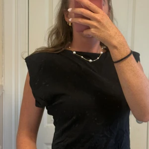 Svart t-shirt från Josefine HJ x NA-KD - Svart t-shirt med axelvaddar från Josefine HJ x NA-KD med boxig passform och markerade axlar. T-shirten har korta ärmar och är tillverkad i mjuk bomull. Enkel och stilren design som passar perfekt till jeans eller kjol.