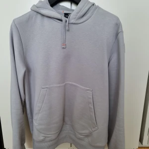 Stone blue hoodie från Parajumpers - Snygg ljusgrå hoodie från Parajumpers med broderad patch på ärmen, känguruficka och half zip framtill. Hoodien har långa ärmar och coola röda sömdetaljer längs axlarna. Perfekt för dig som gillar streetwear och vill ha något bekvämt och stilrent.