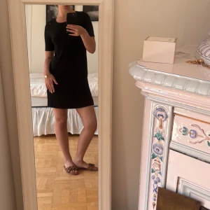 Svart kortärmad strand klänning - Enkel och stilren svart klänning i kort modell med rund halsringning och korta ärmar. Klänningen har en rak passform och är tillverkad i mjukt bomullstyg, perfekt för en avslappnad och perfekt till stranden