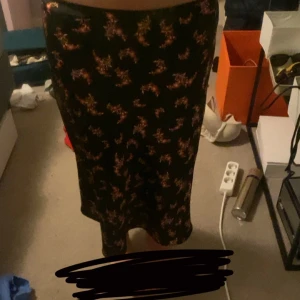 Svart långkjol med blommigt mönster - Svart satin långkjol med små blommiga mönster i rosa och orangea toner. Jag är cirka 175cm 