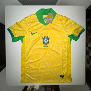 Nike x Brasilien fotbollströja - Säljer en officiell Brasilien fotbollströja från Nike i storlek S. Tröjan är gul med gröna detaljer och har ett unikt grafiskt mönster över hela tyget. Klassisk krage i grönt, CBF-emblem på bröstet och Nike-logga. Tillverkad i lätt och ventilerande material.