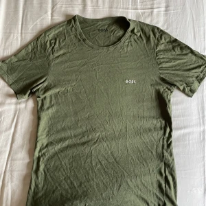t-shirt Hugo boss  - Snygg olivgrön t-shirt från BOSS med diskret broderad logga på bröstet. Klassisk rund halsringning och korta ärmar. Tillverkad i mjuk bomull som känns skön mot huden. Perfekt för en clean och stilren look. Legat i garderoben sen jag köpte så därför skrynklig 