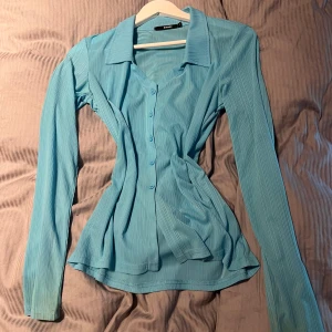 Blå ribbad skjorta från Bik Bok - Snygg ljusblå skjorta från Bik Bok med ribbad struktur och klassisk krage. Skjortan har lång ärm, knappar framtill och figurnära passform. Perfekt för dig som gillar stilrena och trendiga plagg med lite extra detalj. Lite missfärgad i ärmarna men inget man tänker på vid användning