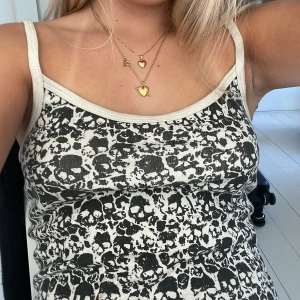 Svartvit linne med dödskallemönster - Cool linne med smala axelband och svartvitt dödskallemönster över hela toppen. Ljus kant runt halsringning och ärmhål. Perfekt för dig som gillar edgy och alternativ stil. Mjuk och stretchig bomullskänsla, sitter tajt och croppad på kroppen.