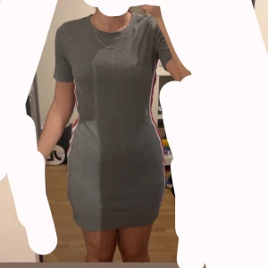 Grå tight kortklänning H&M - grå tight kortklänning från H&M. Klänningen har korta ärmar och coola rosa och vita ränder längs sidorna. Den är figurnära och stretchig, perfekt om du gillar sportig och enkel stil. Använd 2 ggr. Storlek M. Passar S oxå. 