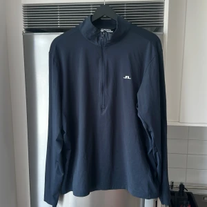Golftröja J.Lindeberg Large  - Snygg marinblå långärmad tröja från J.Lindeberg med half zip och liten vit logga på bröstet samt en större i nacken. Använd två gånger kanske. 