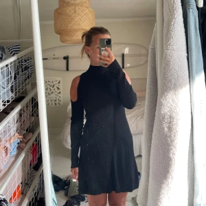 Svart ribbad klänning från Zara - Supersnygg svart ribbad kortklänning från Zara med lång ärm och coola cut out-detaljer på axlarna. Hög krage och figurnära passform som ger en stilren vibe. Aldrig använd, som ny.