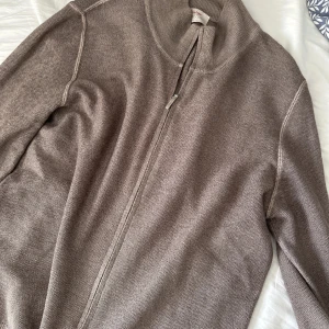 Beige kofta från Gran Sasso - Snygg beige kofta från Gran Sasso med hel dragkedja och ribbad krage. Tillverkad i ett tunt, stickat material som känns lyxigt. 