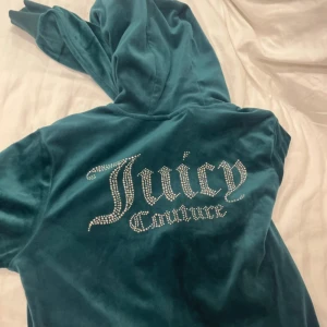Juicy Couture velour hoodie och byxor, grön - Juicy Couture hoodie i smaragdgrön velour med huva och glittrande strasstenar på ryggen och bröstet. Klassisk zip-up modell med ribbade muddar och snyggt broderad logga. Perfekt för dig som vill ha den ikoniska Y2K-looken.