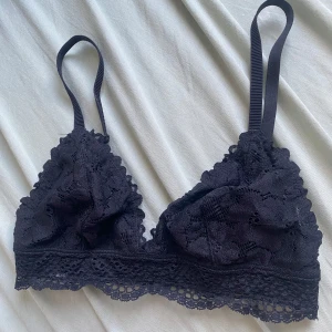 Svart spets bralette med justerbara band - Supersöt svart bralette i spets med tunna, justerbara axelband och bred spetskant nedtill. Triangelkupor med blommigt spetsmönster och hakknäppning bak. 