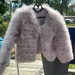 Ljuslila pälsjacka från DennisM - Supermjuk och fluffig ljuslila pälsjacka från DennisM. Jackan är croppad med lång ärm och har quiltat, glansigt foder på insidan. Perfekt för dig som vill sticka ut med en cozy och trendig look.