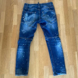 Dsquared2 blå distressed jeans - Snygga blå jeans från Dsquared2 med slitningar lätt att styla med valfri tröja (vitt, blått,svart osv), hål och vita färgstänk för en trendig look. Klassisk femficksmodell med slim fitt och lite pös hela vägen. Perfekta för dig som gillar streetstyle och vill sticka ut. Pris kan diskuteras vid snabb affär. Kan mötas upp i Stockholms området🤩💸