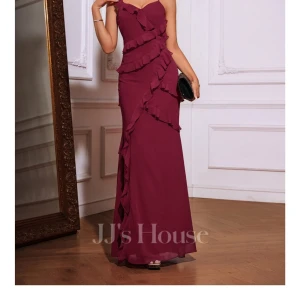 Vinröd långklänning med volanger - Supersnygg vinröd långklänning från JJ's House med tunna axelband, v-ringning och volangdetaljer som går diagonalt över hela klänningen. Öppen rygg med knyt och slits framtill. Perfekt för bal eller fest! Materialet känns lätt och flowy.