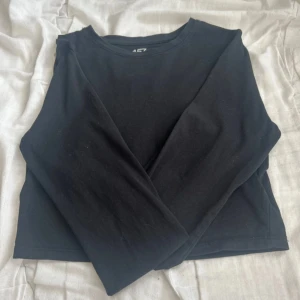Svart croppad topp i bomull - Enkel svart croppad topp från lager 157 i mjuk bomull med lite stretch. Modellen är långärmad och har rund halsringning, perfekt att styla med jeans eller kjol. Materialet är 95% bomull och 5% elastan för en bekväm passform.
