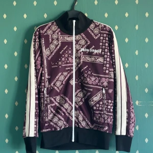 Palm Angels Track Jacket Bandana - Palm Angels track jacket i mörklila med bandanamönster och vita detaljer. Jackan har endast blivit använd någon enstaka gång. Materialet är polyester. 
