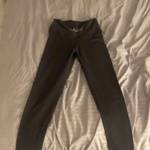Svarta leggings från Gavelo - Svarta leggings från Gavelo med hög midja och snyggt broderad logga både fram och på benet. Tillverkade i stretchigt syntetmaterial som sitter tight och bekvämt. Perfekta för träning eller chill, med scrunch-detalj bak för extra passform.