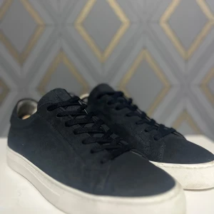 Marinblåa sneakers med vit sula från Björn Borg  - Snygga marinblåa sneakers från björn Borg med en stilren design och vit sula. Typ aldrig använda Skorna har snörning och är tillverkade i mocka för en lyxig känsla. Perfekta för en avslappnad men ändå trendig look.