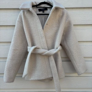 Beige kappa från Veromoda - Säljer en beige kappa från Veromoda. Den har knappar som man kan stänga jackan med men även ett band. Det är alpacka material. Använd en gång. 