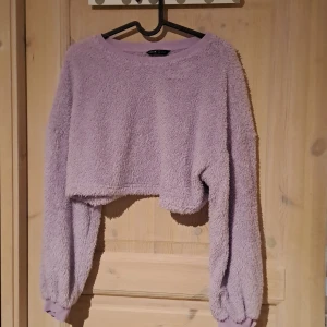 Lila fluffig croppad tröja från Shein - Mysig lila croppad tröja från Shein i ett fluffigt material. Tröjan har långa ärmar och ribbade muddar vid ärmslut och hals. Perfekt för en avslappnad stil.