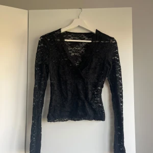 Svart spetsblus - Säljer en elegant svart spetsblus med långärmad design. Blusen har ett vackert blommönster och en v-ringad hals. Dock är den lite trådig, därav är priset sänkt (original pris runt 299)