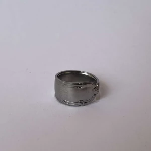 Silverfärgad ring - Elegant silverfärgad ring med en stilren och modern design. Ringen har en slät yta med subtila detaljer som ger den en unik karaktär. Perfekt för att komplettera din stil med en touch av elegans.