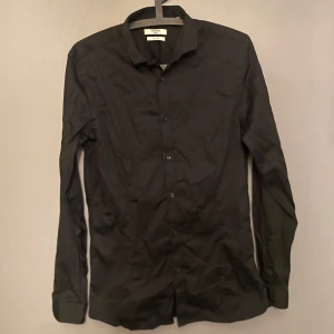 Svart skjorta från Jack & Jones - Snygg svart skjorta från Jack & Jones i storlek M. Skjortan har långa ärmar och knappar framtill. Perfekt för en stilren look.
