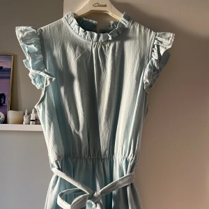 Ljusblå klänning med volangdetaljer - Charmig ljusblå klänning med volangdetaljer vid ärmarna och halsen. Klänningen har en knytning i midjan och en luftig, flerdelad kjol. Perfekt för en somrig look! Knappt använd💕
