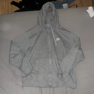 Grå hoodie från Nike - Säljer en grå hoodie från Nike med dragkedja och huva. Perfekt för en avslappnad stil. Den har en klassisk Nike-logga på bröstet och är tillverkad i mjukt material för extra komfort.