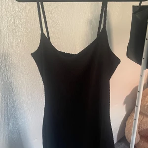 Svart klänning med smala axelband - Snygg svart klänning med smala axelband och en texturerad yta. Perfekt för en stilren look. Klänningen har en enkel design som gör den lätt att matcha med olika accessoarer.