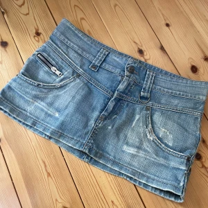 Blå jeanskjol  - Snygg jeanskjol från Einstein i en klassisk blå denim. Kjolen har en kort längd med slitna detaljer och  fickor fram och bak. Den har en knapp och dragkedja framtill samt bälteshällor. Perfekt för en avslappnad stil. Den är 39 cm tvärs över. 