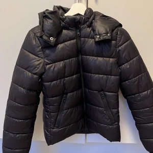 Svart pufferjacka från Gina Tricot - Säljer en svart pufferjacka från Gina Tricot med huva och dragkedja. Jackan har en quiltad design och är perfekt för kyligare dagar. Den har långa ärmar och en stilren look. Passar även bra för höst och våren. Vi kan även snacka för ett bättre pris❣️