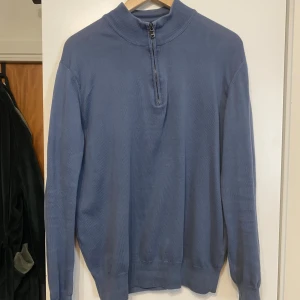Blå tröja med dragkedja från Oscar Jacobson - Säljer en stilren blå tröja från Oscar Jacobson med halv dragkedja vid halsen. Tröjan har långa ärmar och en ribbad krage. Perfekt för en avslappnad men ändå elegant look. Storlek S, tror original pris är 1500kr
