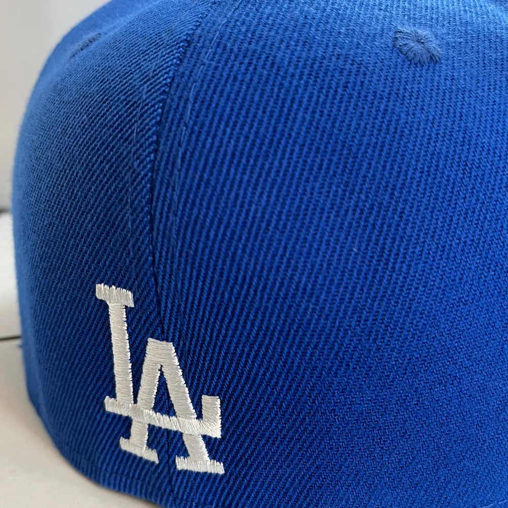 Snygg blå keps från New Era med broderade blommor och LA-logga framtill. Kepsen har en platt skärm och en broderad detalj på sidan med texten 'World Series'. Perfekt för att ge din outfit en sportig touch!. Asusteet.
