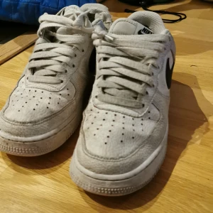 Vita Nike Air Force sneakers - Tja! Säljer ett par klassiska vita Nike Air Force sneakers med svart Nike-logga. Perfekta för en avslappnad stil. Har använt skorna väldigt mycket så det är inte i ett jättebra skick men det ska nog gå att få det se nyare iallafall. Hör av dig om du vill köpa. Nypris: 1350 kr