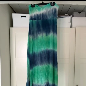 Grön och blå långklänning från Paper Scissors - Säljer en färgglad långklänning från Paper Scissors i grönt och blått. Klänningen har ett unikt mönster och är perfekt för sommarens varma dagar. Den är ärmlös och har en luftig passform. Nice till stranden och man kan ha den som en lång kjol också och vika ner den övre delen