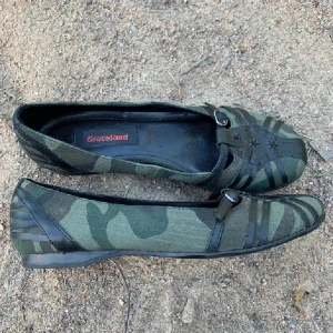 Camouflagefärgade ballerinaskor från Graceland - Snygga ballerinaskor i camouflagefärg från Graceland. Skorna har ett dekorativt blommönster och remmar med spänne över foten. Perfekta för en avslappnad stil med en touch av edge.