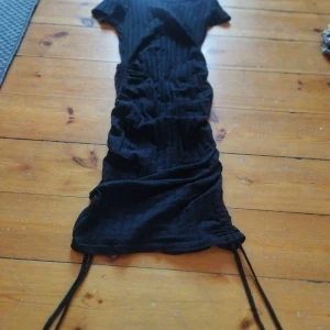 Svart ribbad klänning - Snygg svart ribbad klänning med korta ärmar och knytband i sidorna. Perfekt för en stilren look. Klänningen har en åtsittande passform och är gjord i ett mjukt material.