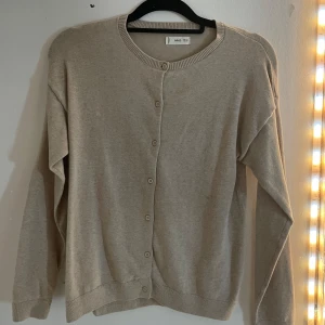 Beige kofta från MNG - Säljer en stilren beige kofta från MNG med knappar framtill. Perfekt för lager-på-lager och passar till många olika outfits. Koftan har långa ärmar och ribbade kanter för en klassisk look.