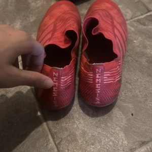 Röda fotbollsskor från Adidas - Säljer ett par röda Adidas fotbollsskor med en stilren design och de klassiska tre ränderna på sidan. Skorna har en strumpliknande passform utan snörning för en smidig känsla på planen.