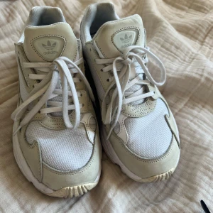 Vita sneakers från Adidas - Säljer ett par vit/beiga sneakers från Adidas med klassisk design och snörning. Perfekta för vardags eller när man är ute och går. Äldre modellen av adidas Falcon. 